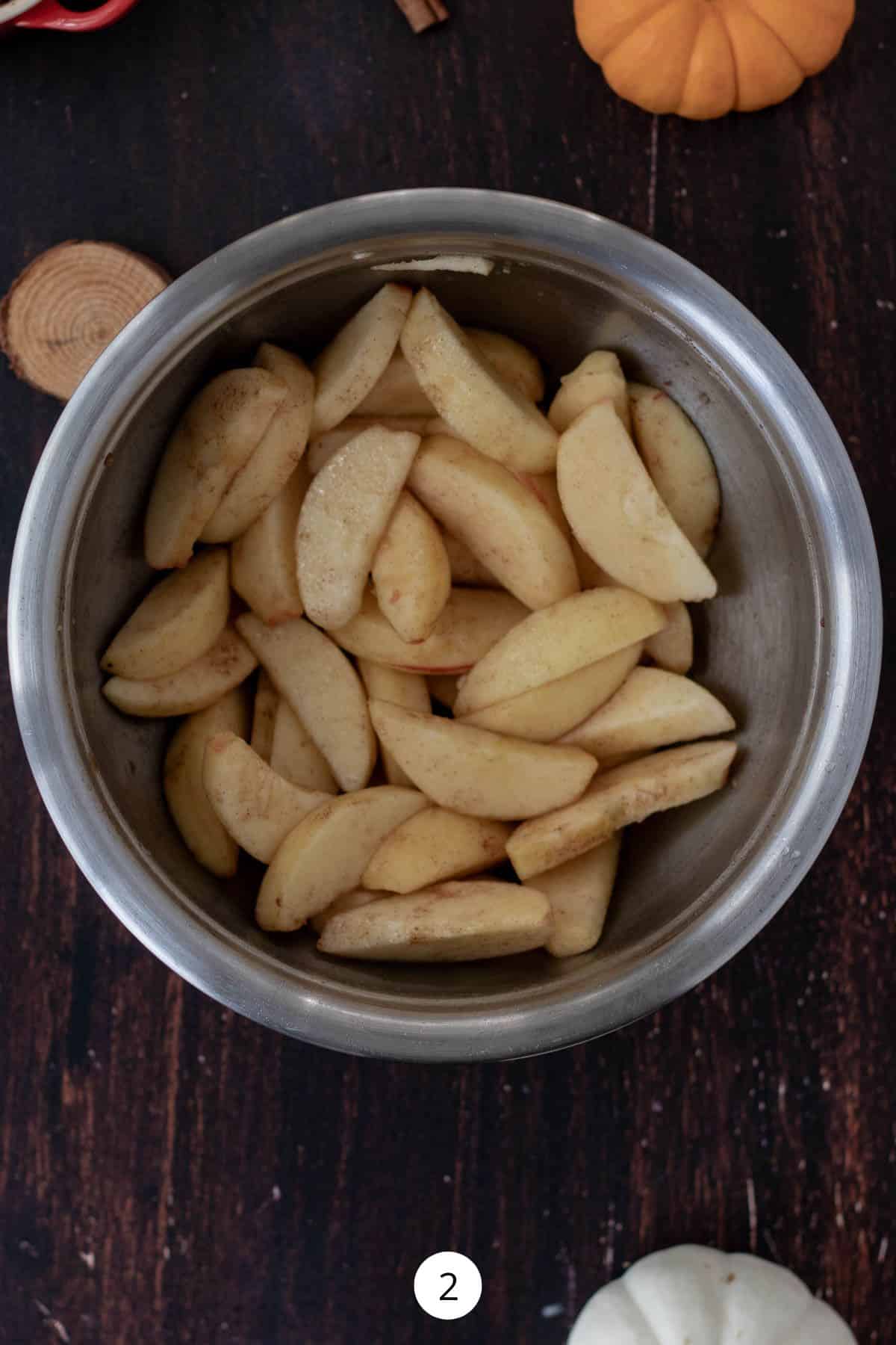 Peeled apples tossed with cinnamon in a small stainless-steel bowl.