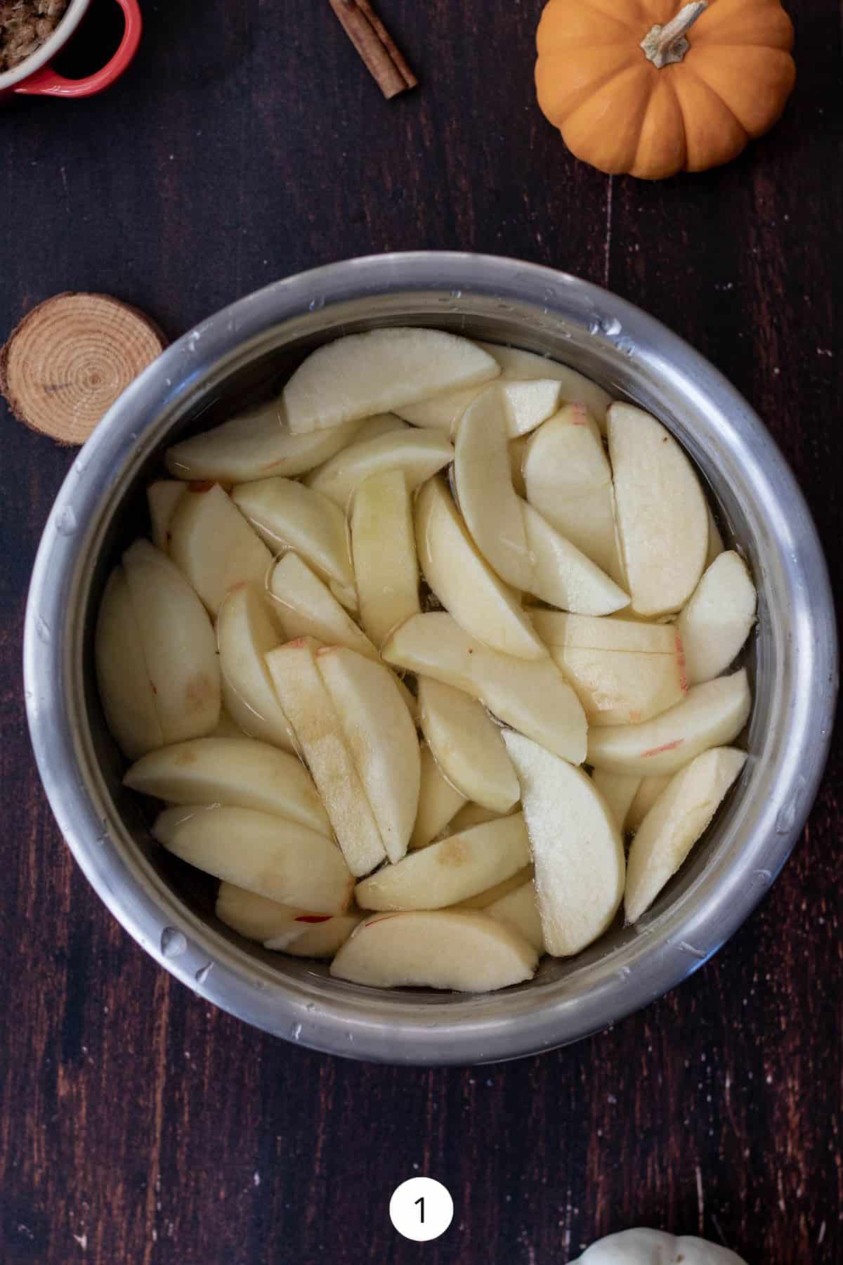 Peeled and sliced apples in a small stainless-steel mixing bowl.