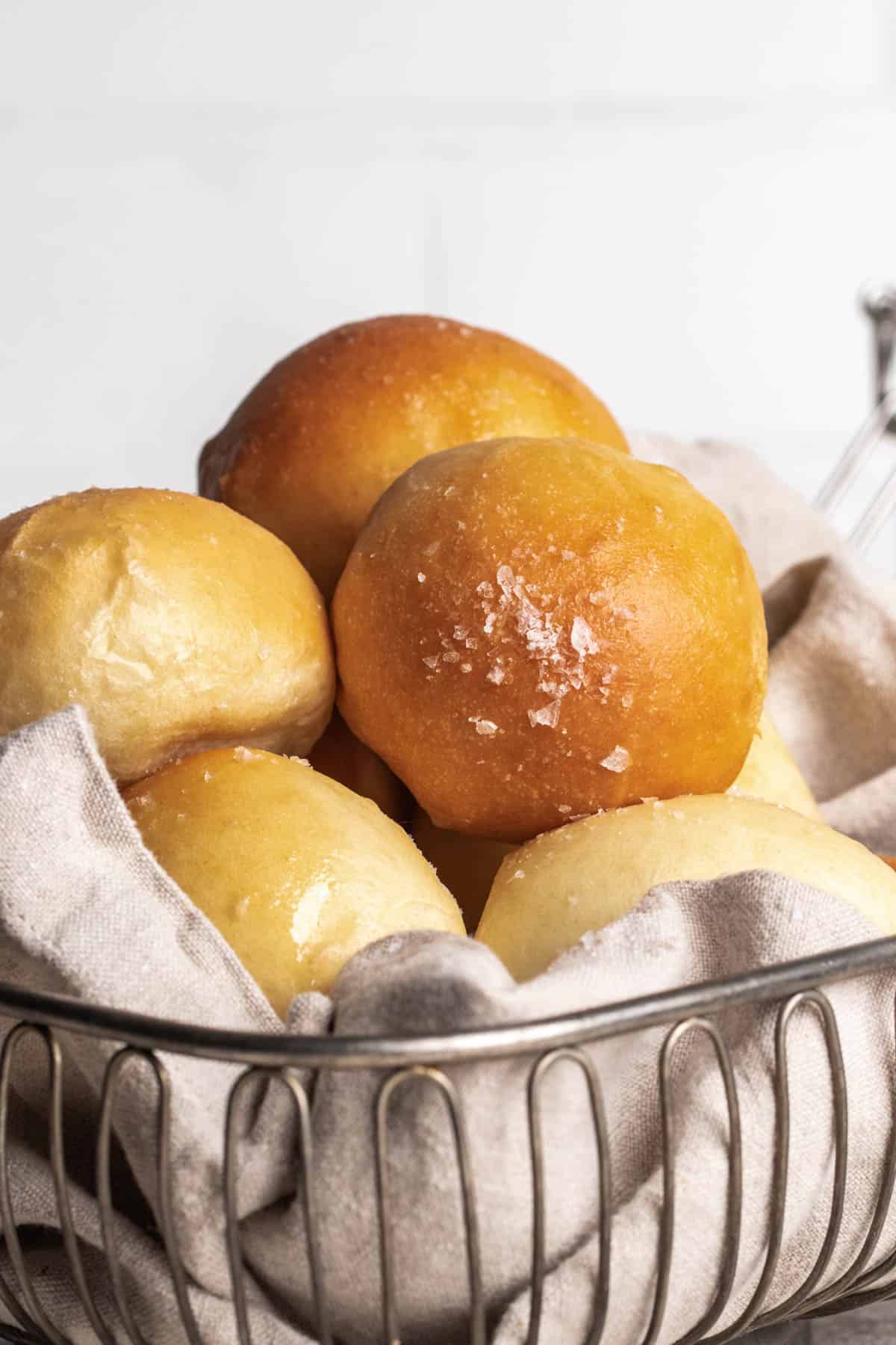 Bread rolls stacked high inside of a wire bread basket lined with a grey napkin.