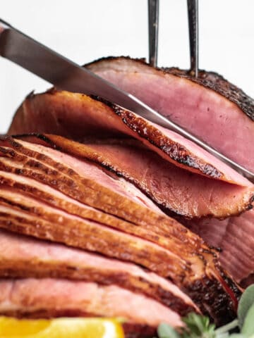 Slicing a glazed ham with a carving knife and fork.