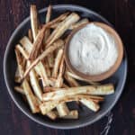 Air-fried parsnips on a dark-grey round plate with a side of aioli sauce.