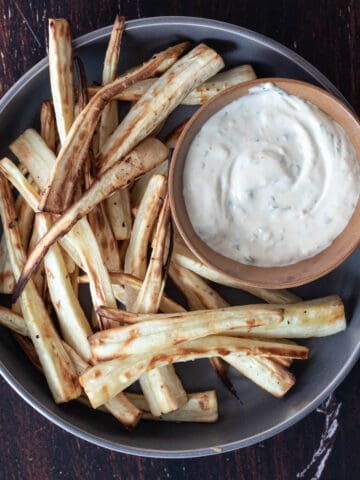 Air-fried parsnips on a dark-grey round plate with a side of aioli sauce.