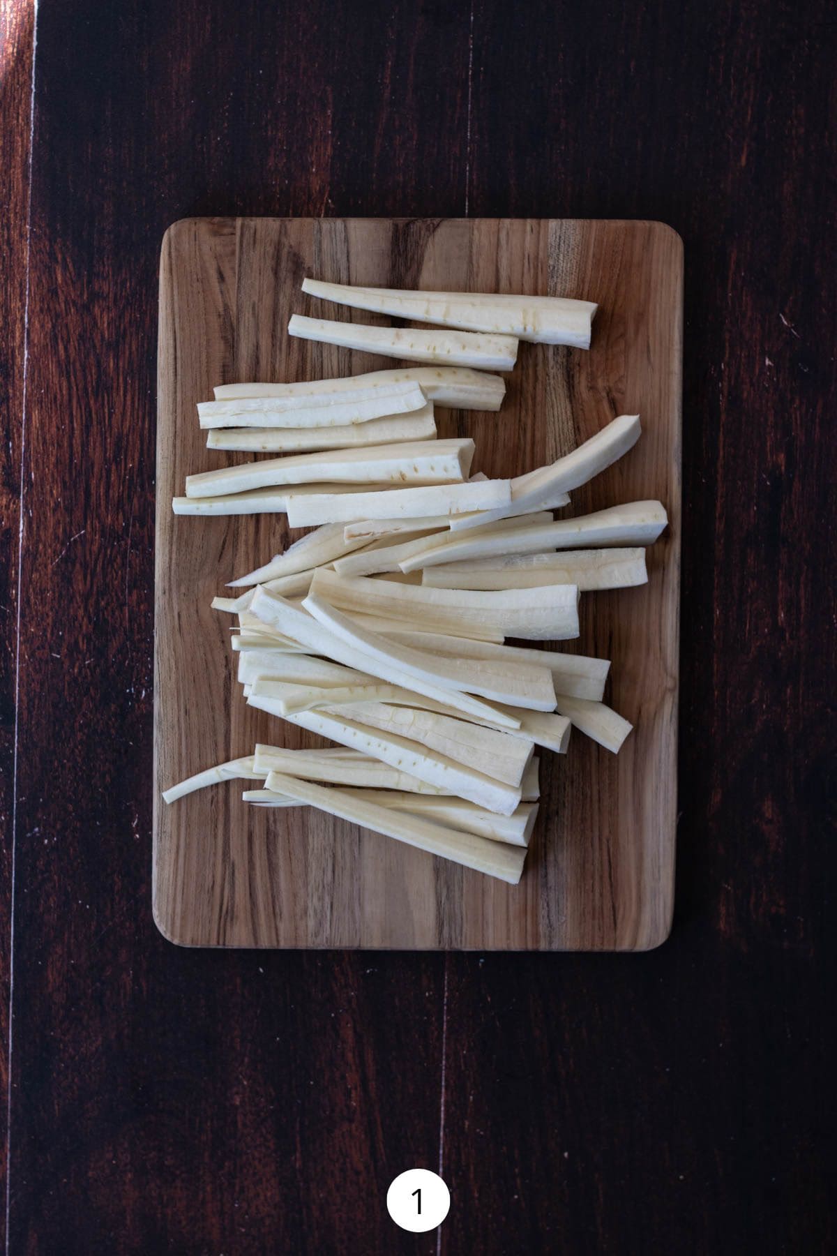 Parsnips cut into sticks on a rectangle wood cutting board.