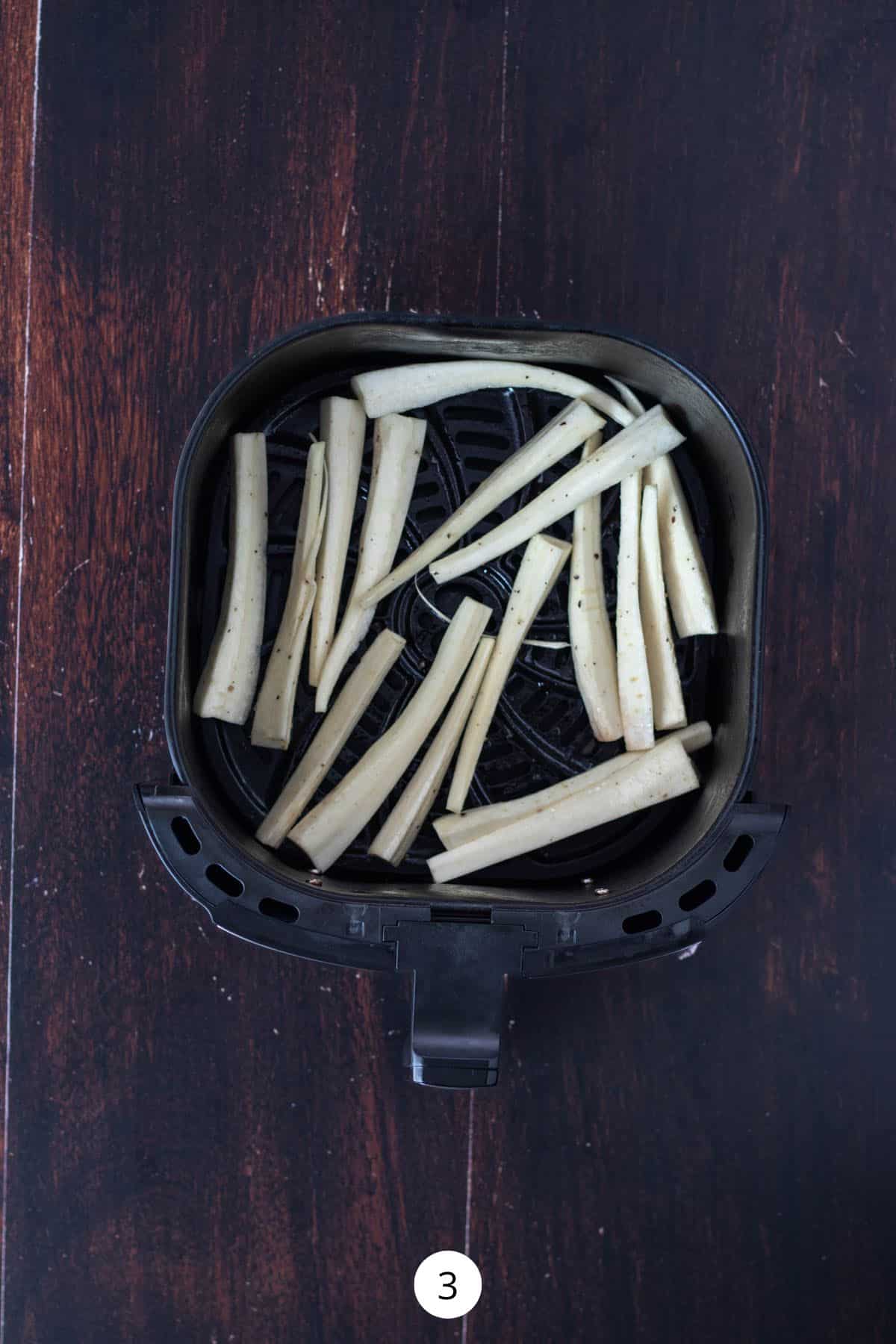 Seasoned parsnip sticks inside of an air fryer basket.