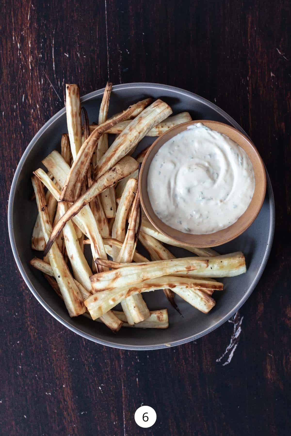Air-fried parsnips inside of a round plate with a small cup of aioli sauce.