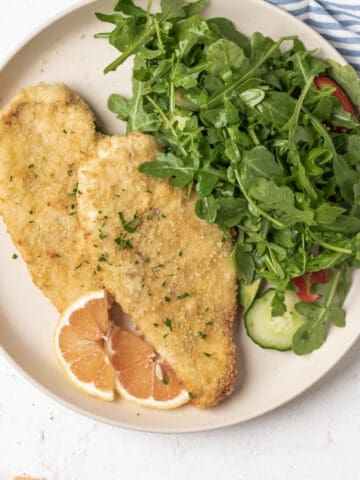 Two breaded and crispy chicken breast served with a arugula salad.