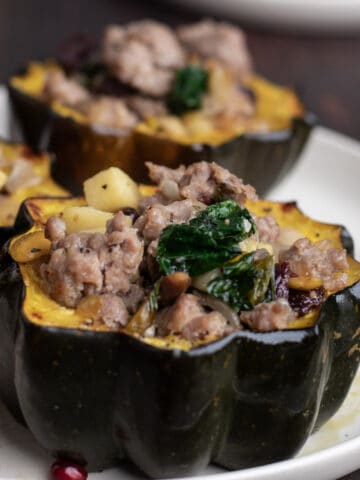 Sausage, apple, and kale stuffed acorn squash halves on a round plate.
