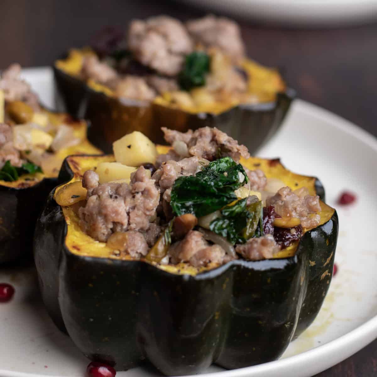 Sausage, apple, and kale stuffed acorn squash halves on a round plate.