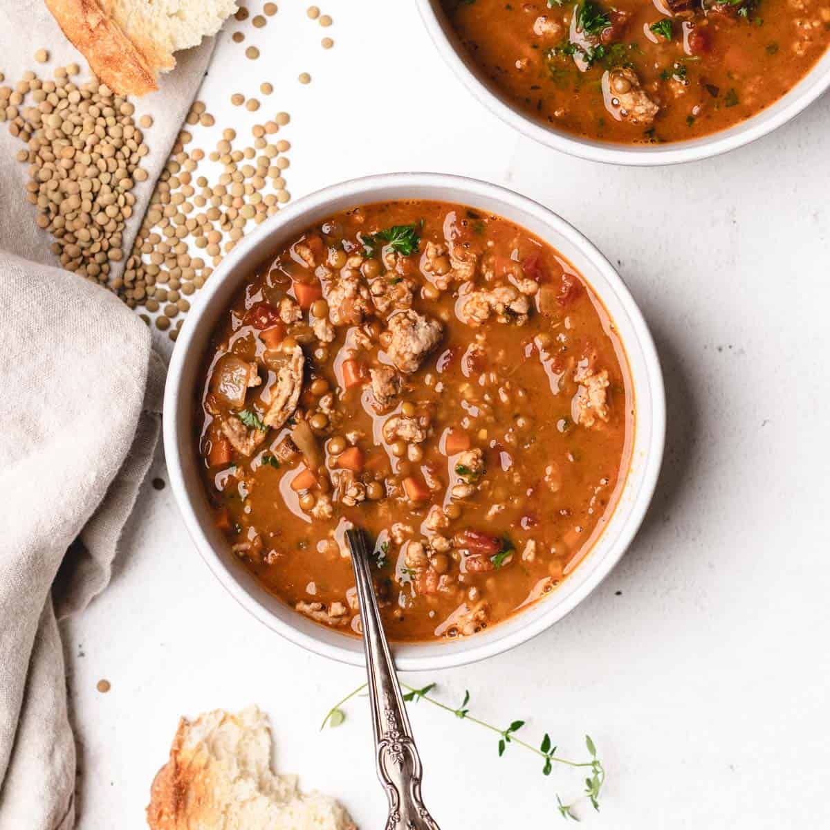 A bowl of turkey lentil soup with dried green lentils scattered around the bowl.