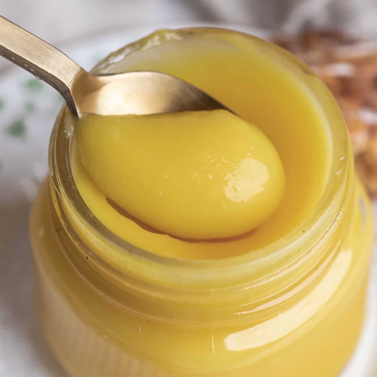 A gold plated spoon inside of a jar of lemon curd.