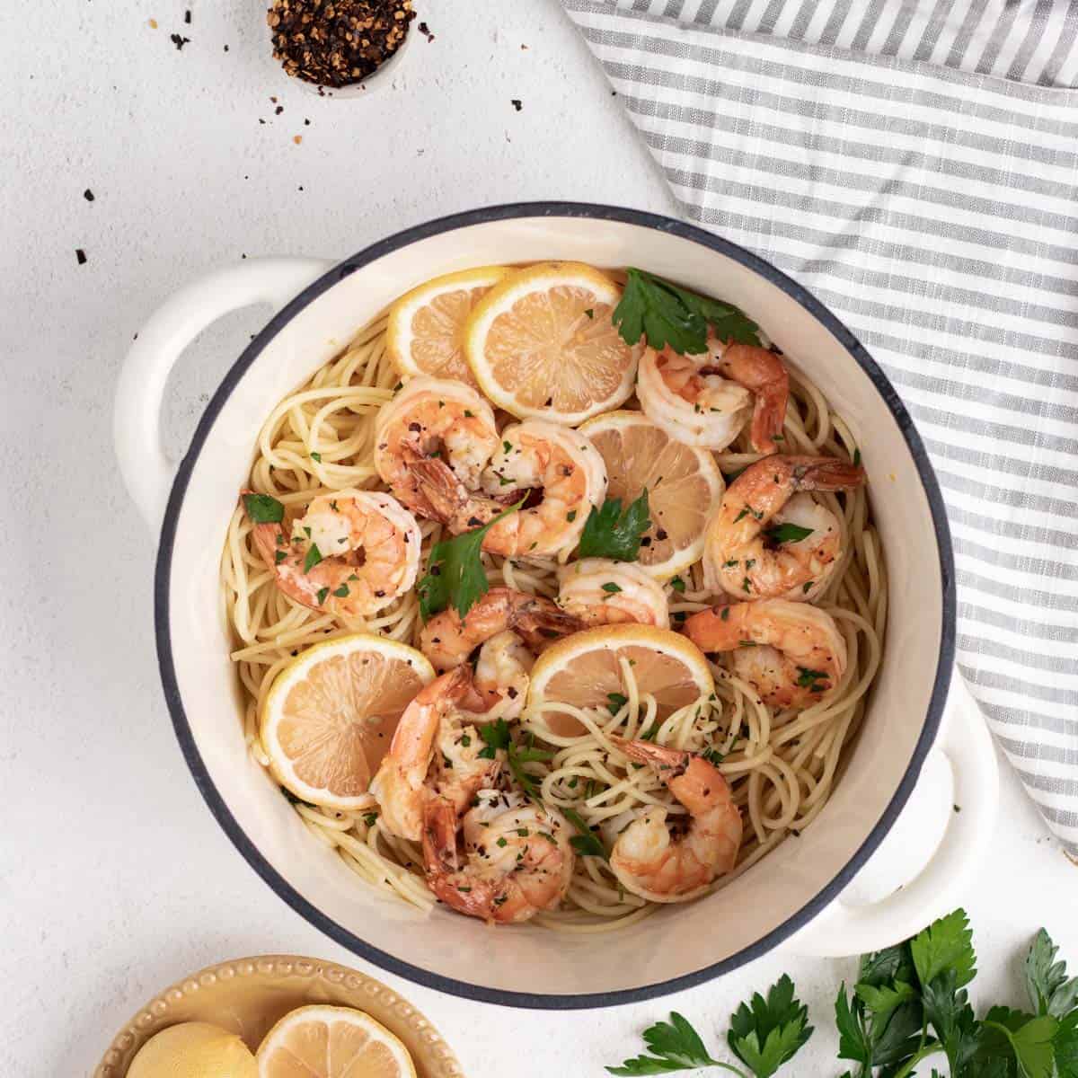 Shrimp scampi with lemon slices and pasta in a white dutch oven.