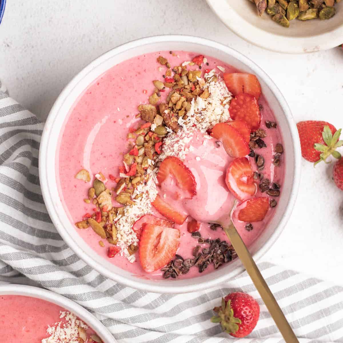 A round bowl with a strawberry smoothie, topping, and a golden spoon.