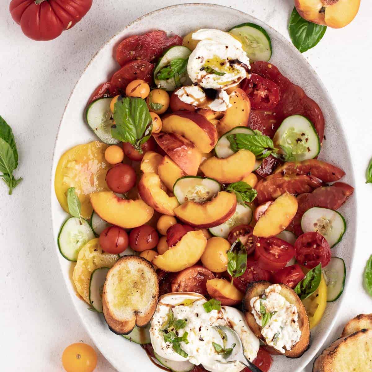 Tomato, peach, and burrata salad on a oval white platter with crusty french bread.