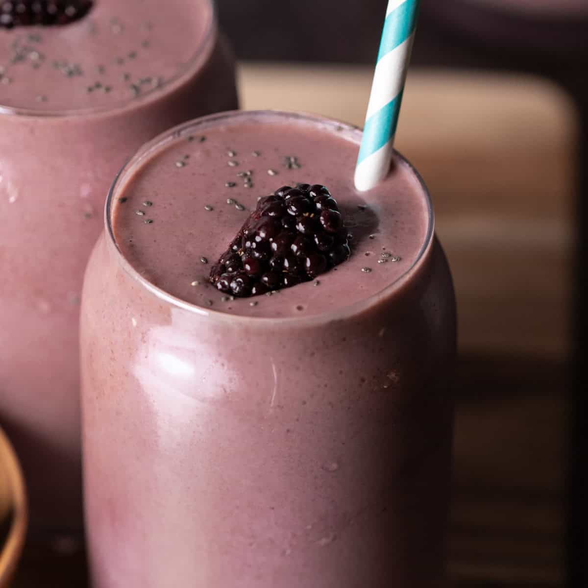 A purple smoothie garnished with chia seeds, blackberries, and paper straw.