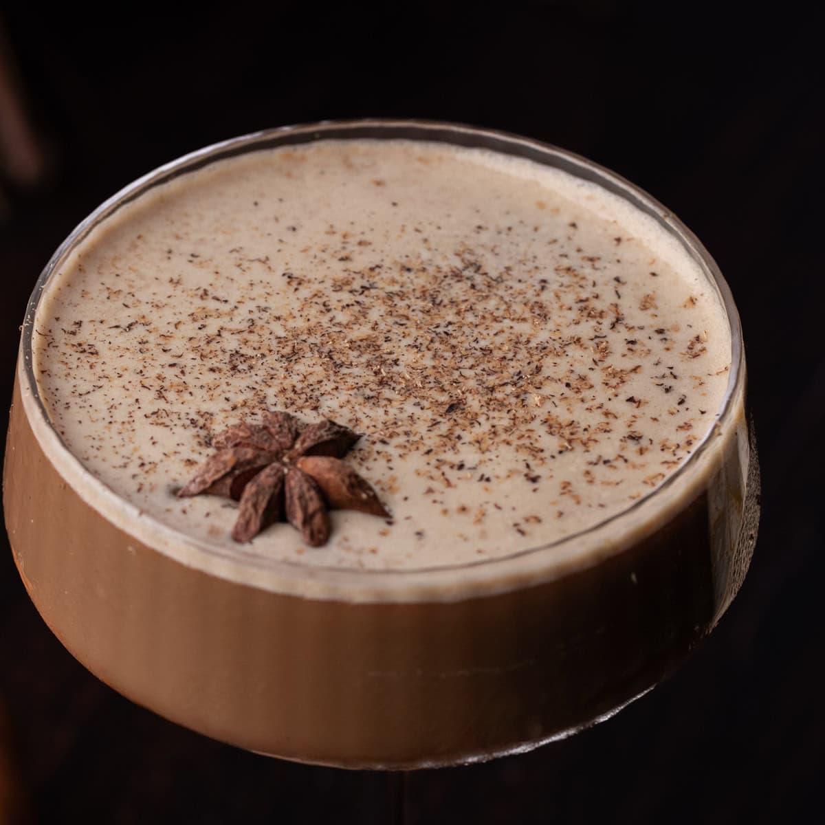 A martini glass filled will a pumpkin espresso martini and garnished with ground nutmeg and one star anise.