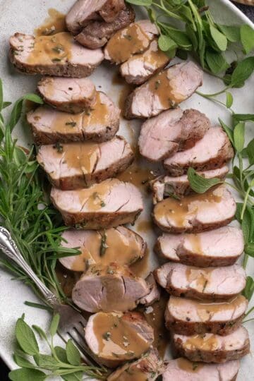 Slice pork tenderloin on a oval platter with a sage cream sauce drizzled over top.