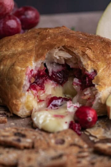 Image of baked brie with a wedge removed, revealing gooey, melted cheese oozing from the center.