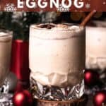 A crystal glass filled with a bourbon eggnog sitting on a wooden coaster and garnished with a cinnamon stick.