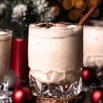 A crystal glass filled with a bourbon eggnog sitting on a wooden coaster and garnished with a cinnamon stick.