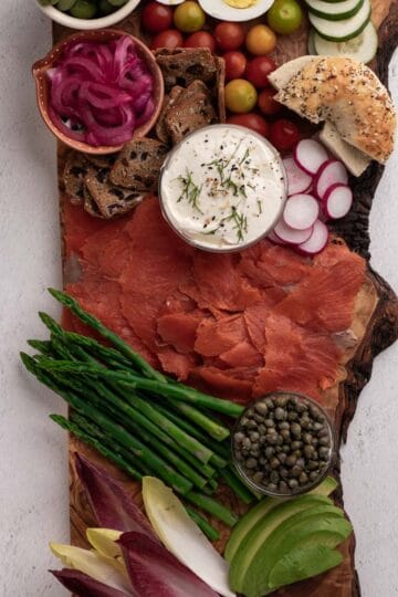 Smoked salmon on a wooden charcuterie board with cream cheese, olives, capers, asparagus, and crackers.