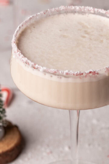 A candy cane rimmed martini glass filled with a White Christmas Cocktail.