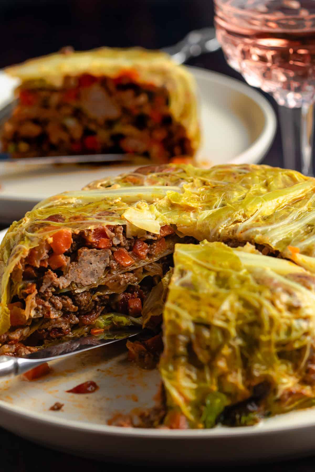 Chou Farci with one slice removed, revealing layers of tender cabbage, and filling on a rustic serving plate.