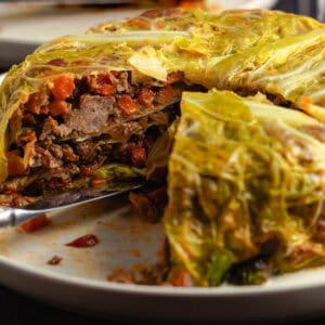 Chou Farci with one slice removed, revealing layers of tender cabbage, and filling on a rustic serving plate.