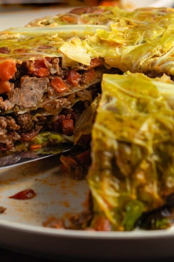 Chou Farci with one slice removed, revealing layers of tender cabbage, and filling on a rustic serving plate.