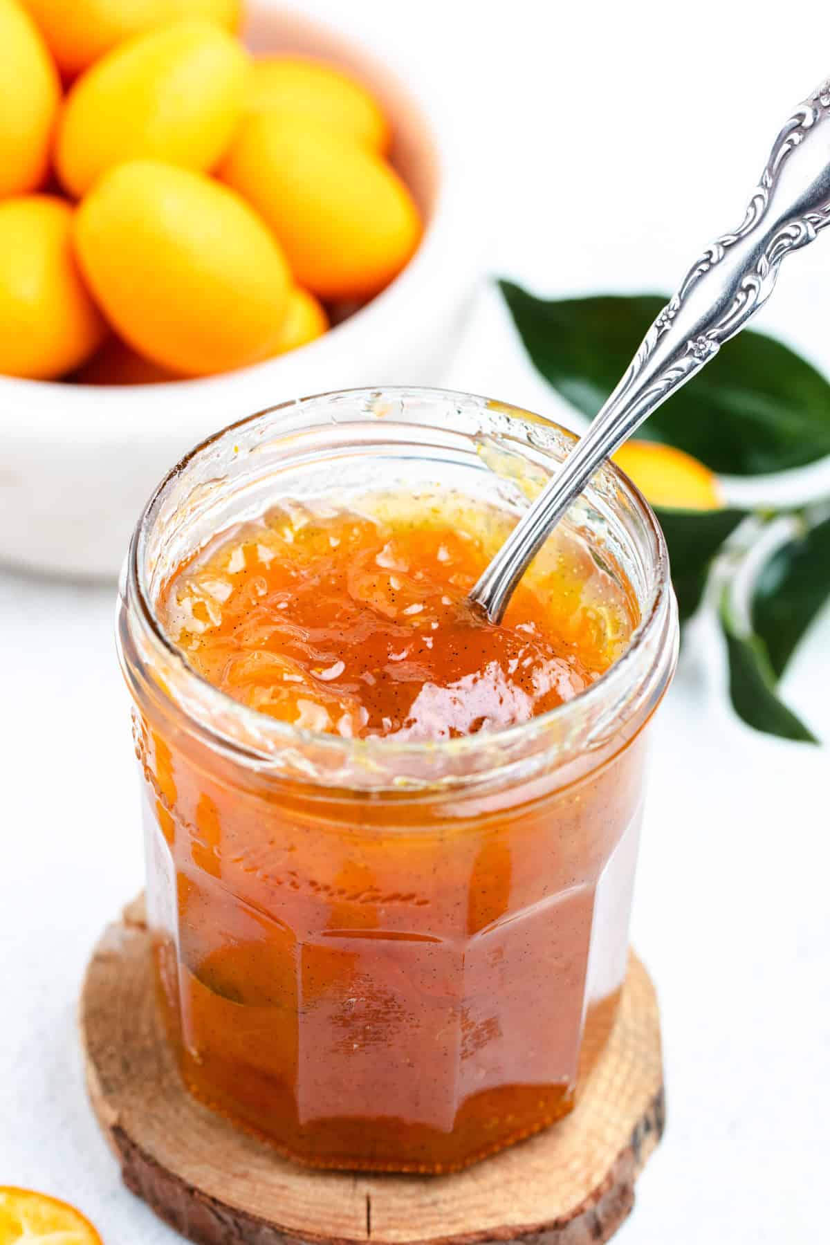 Kumquat jam inside of a glass jar with a spoon.