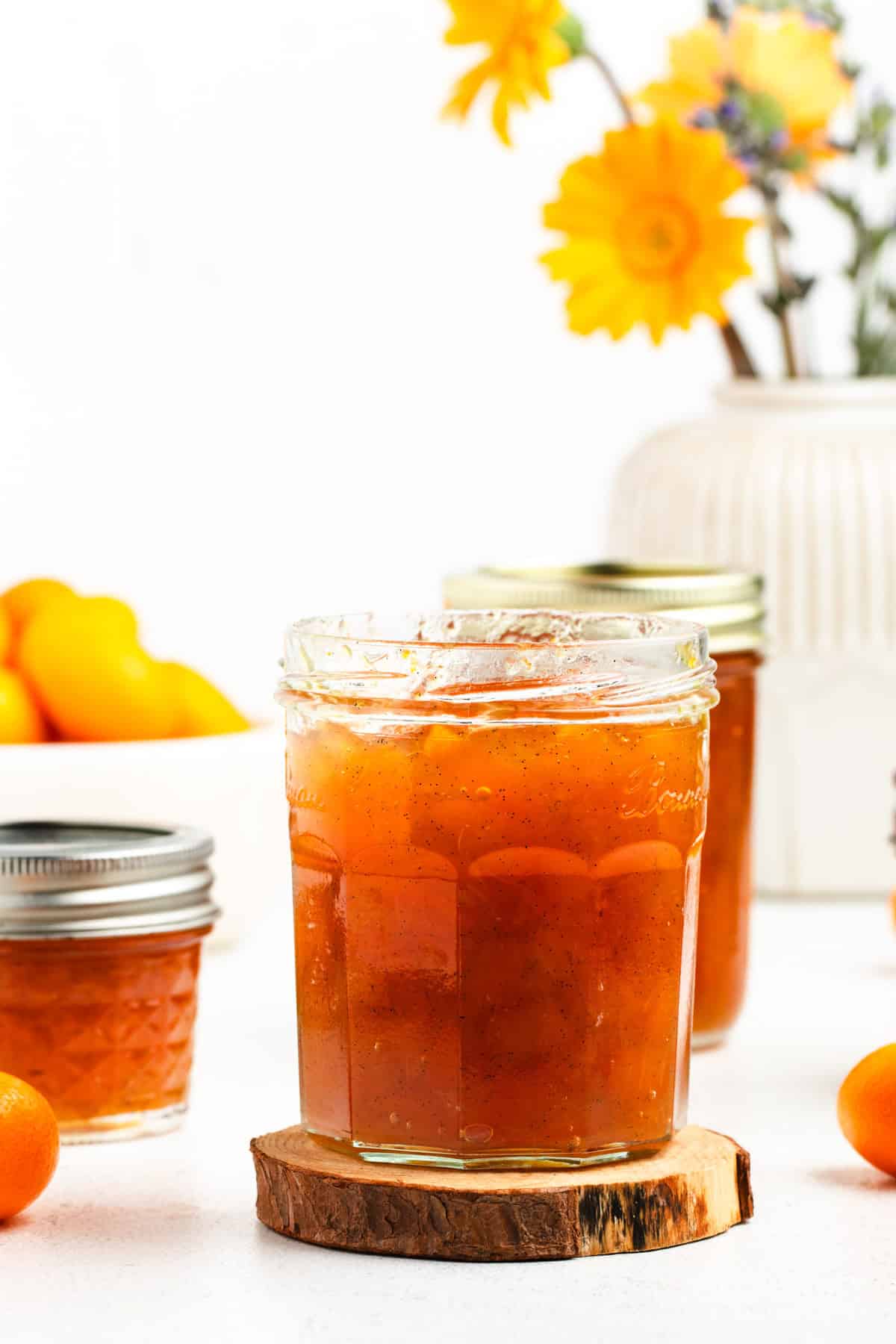 A glass jar filled with kumquat jam sitting on top of a wooden coaster.