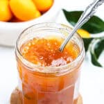 Kumquat jam inside of a glass jar with a spoon.