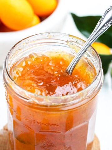 Kumquat jam inside of a glass jar with a spoon.