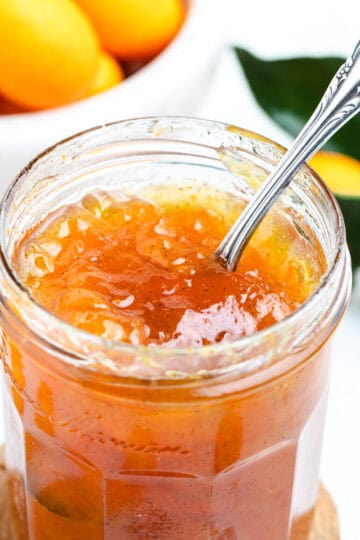 Kumquat jam inside of a glass jar with a spoon.