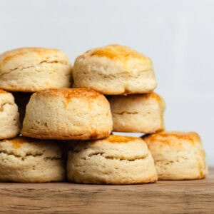 Air fryer scones stacked on top of each other on a wooden cutting board, showing their golden brown tops.
