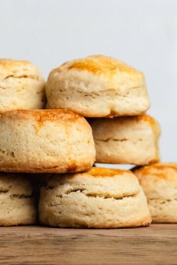 Air fryer scones stacked on top of each other on a wooden cutting board, showing their golden brown tops.
