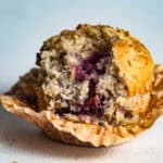 A blackberry muffin resting on a paper muffin liner with a large bite taken out it.