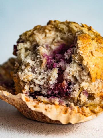 A blackberry muffin resting on a paper muffin liner with a large bite taken out it.