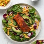 A filet of blackened salmon on top of a salad of leaf lettuce, mango salsa, and sliced avocados.