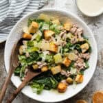 Tuna Caesar salad in a large round white bowl with wooden serving spoons.