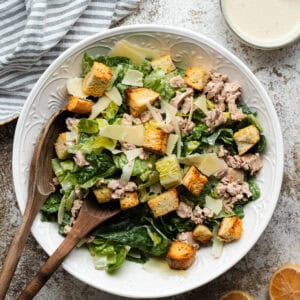 Tuna Caesar salad in a large round white bowl with wooden serving spoons.
