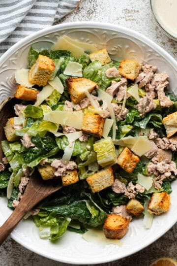 Tuna Caesar salad in a large round white bowl with wooden serving spoons.