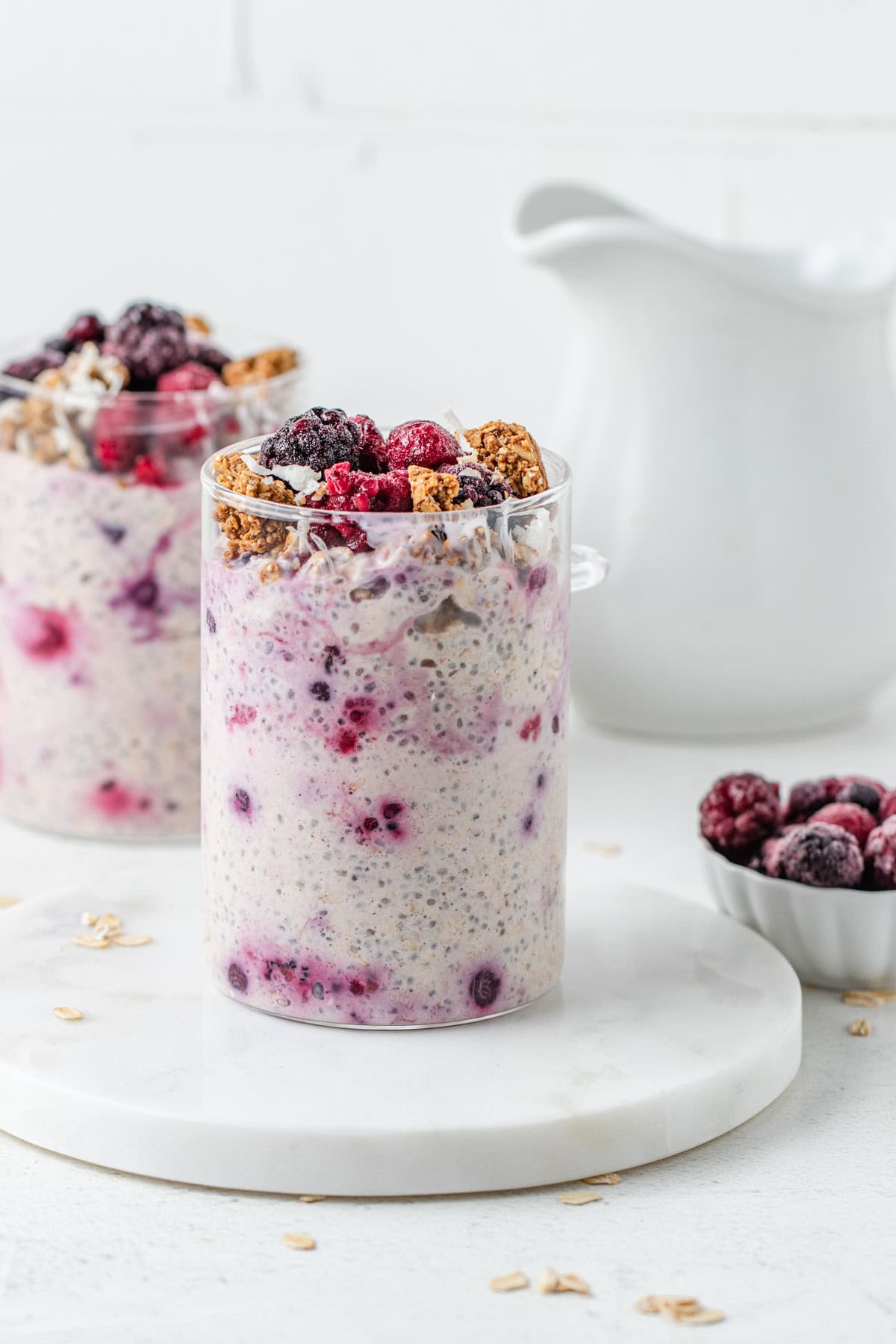 Two glass jars filled with overnight oats and topped with frozen berries and granola.