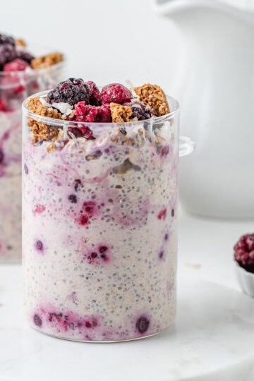 Two glass jars filled with overnight oats and topped with frozen berries and granola.