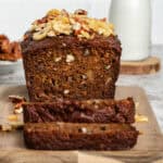 Whole banana bread loaf on a wooden cutting board with two slices placed in front, showing the moist texture and golden-brown crust.