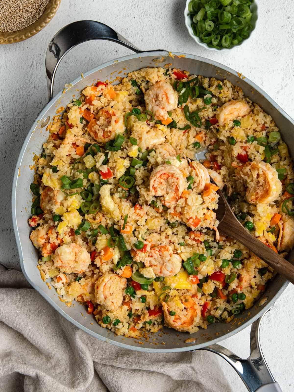 A large pan filled with cauliflower fried rice, garnished with green onions.