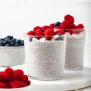 Two glass cups filled with a coconut chia pudding and garnished with fresh berries.