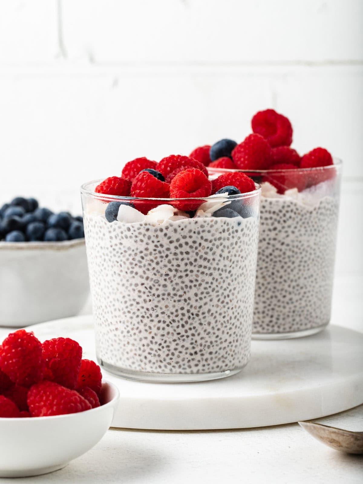 Two glass cups of chia pudding garnished with fresh berries.