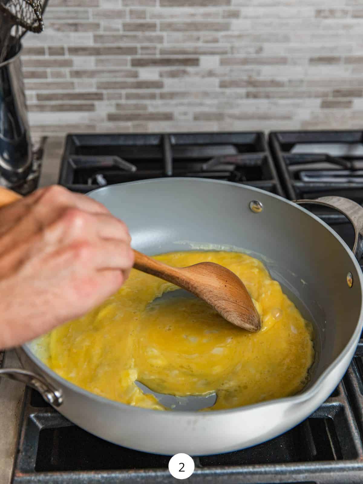 Cooking eggs in a large pan with a wooden spoon.