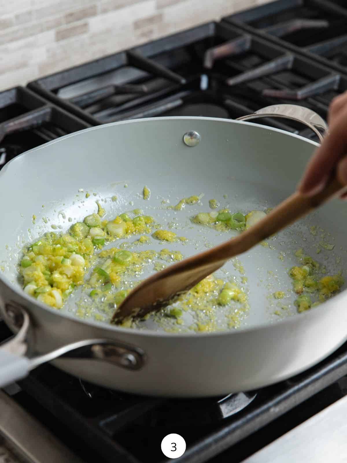 Cooking onions, garlic, and ginger in a large pan with a wooden spoon.