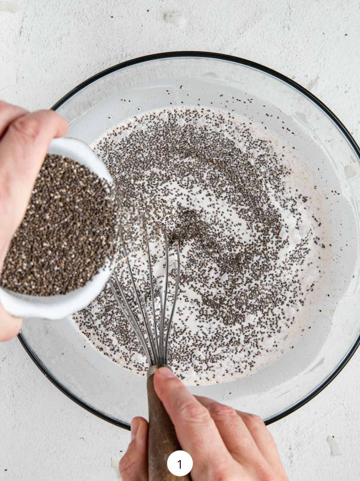 Pouring chia seeds into a mixing bowl with coconut milk and whisking everything together.